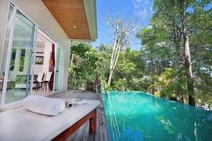 A poolside area with a wooden bench, a towel, and a glass door leading to an indoor space.