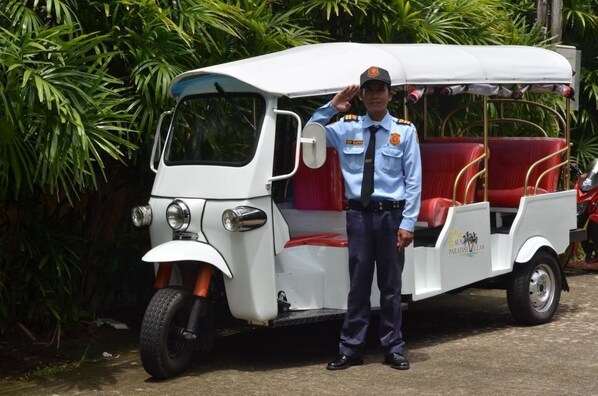 A white three-wheeled vehicle with red seats and a person in uniform standing beside it.