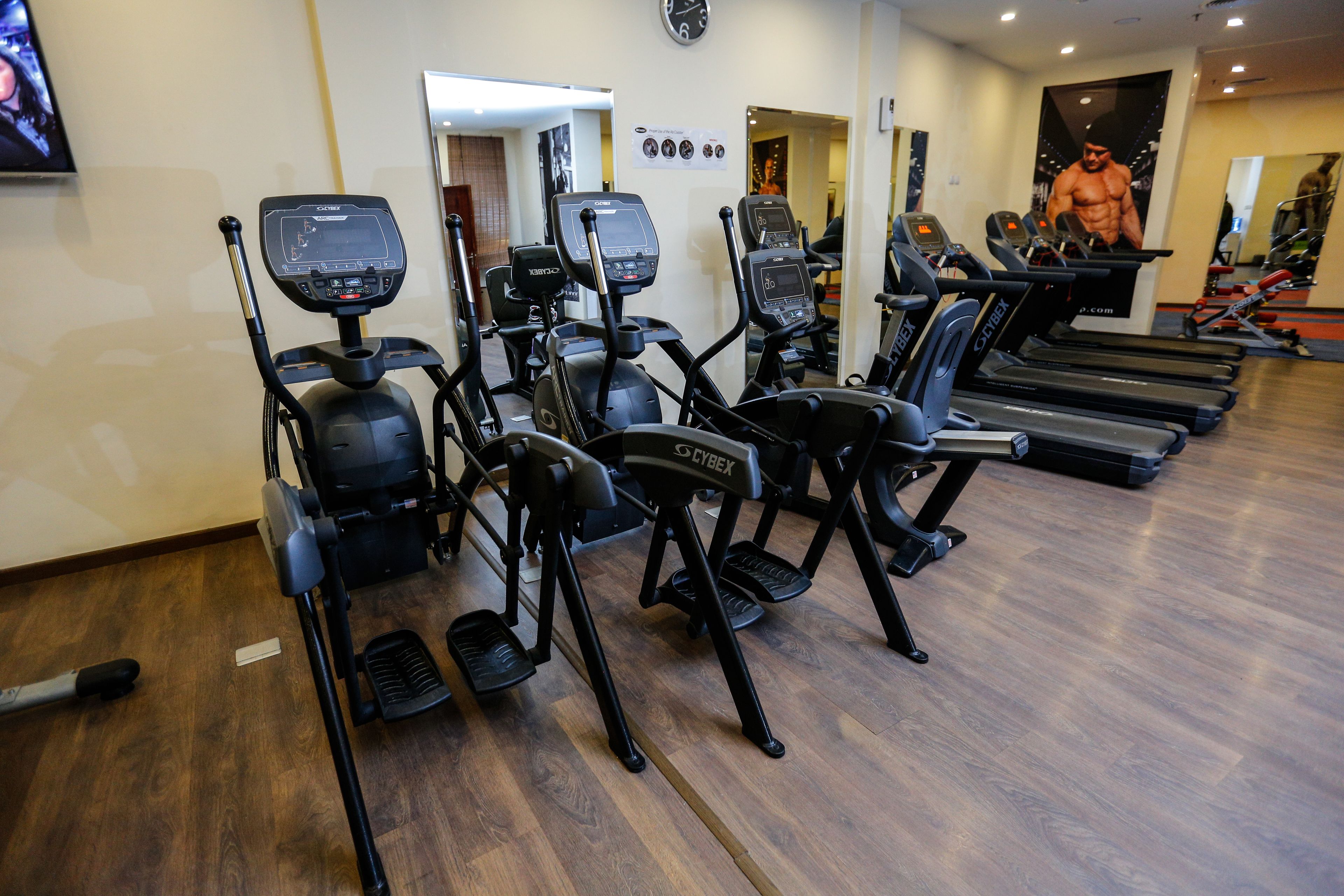 Un gimnasio con cintas de correr y bicicletas estáticas, suelo de madera y un espejo en la pared.