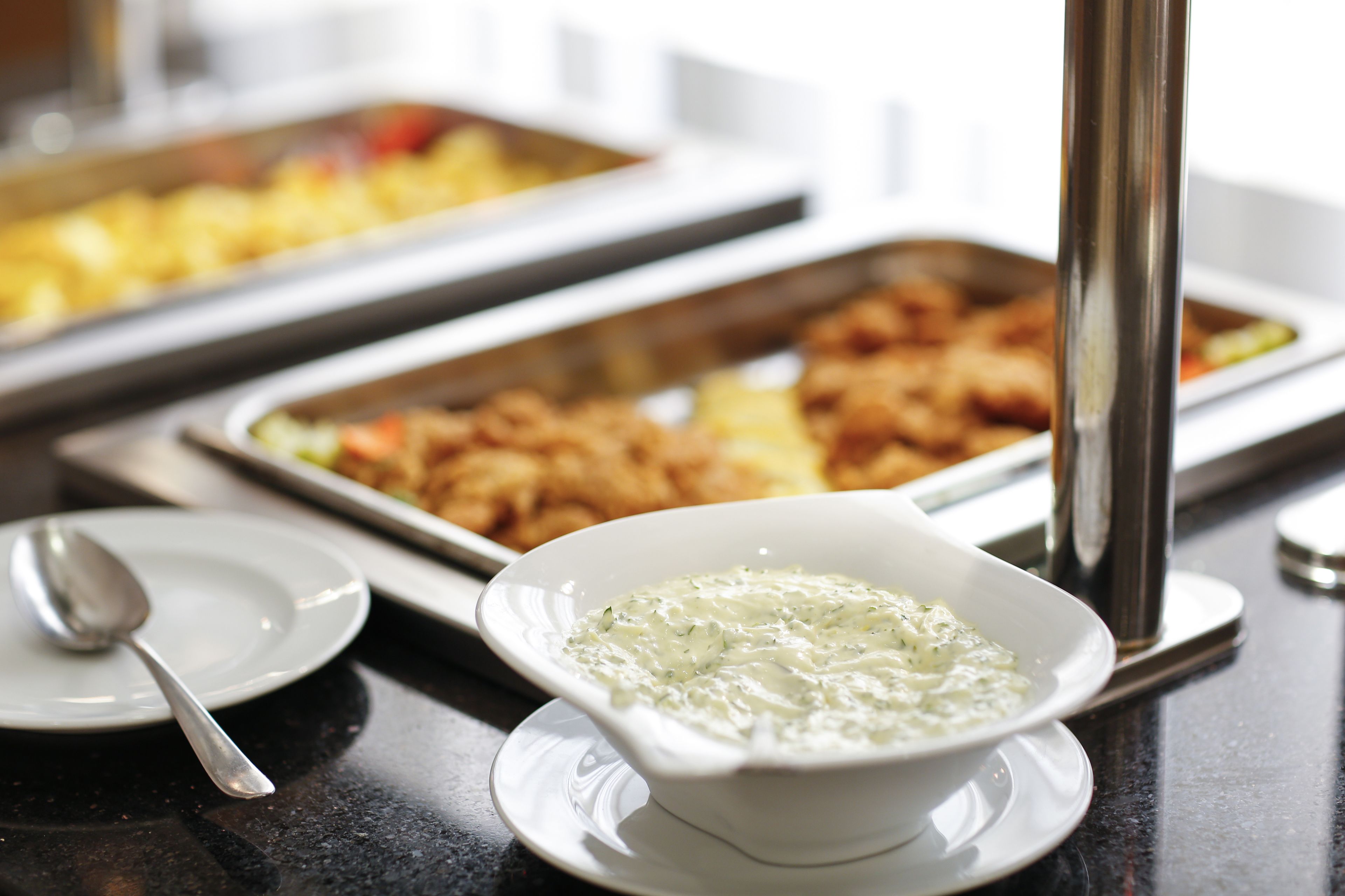 Ein reichhaltiges Buffet mit verschiedenen Speisen, einer Dip-Schale und einem Löffel auf einem Teller.