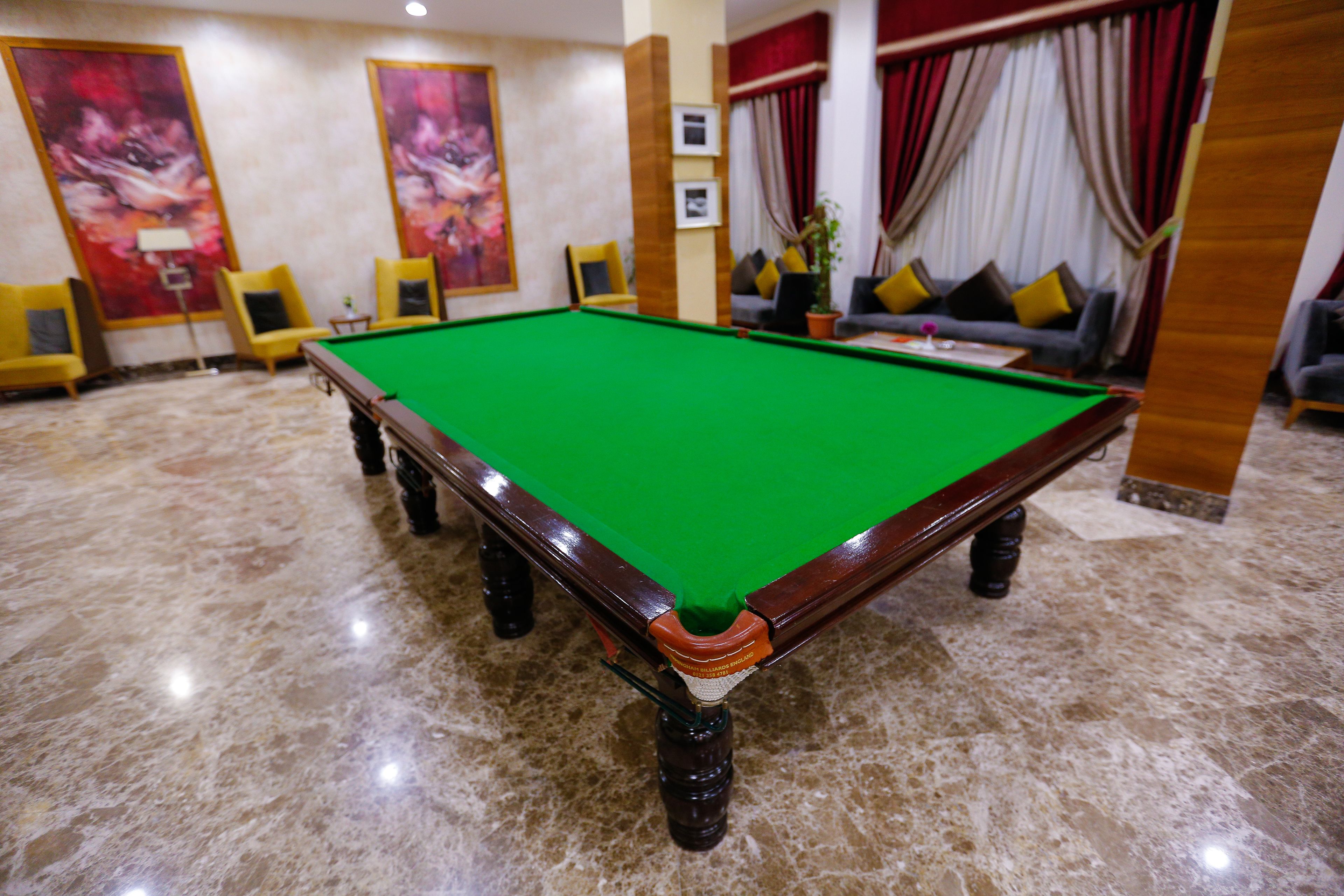 A pool table in a room with a marble floor, yellow chairs, and a sofa with cushions.