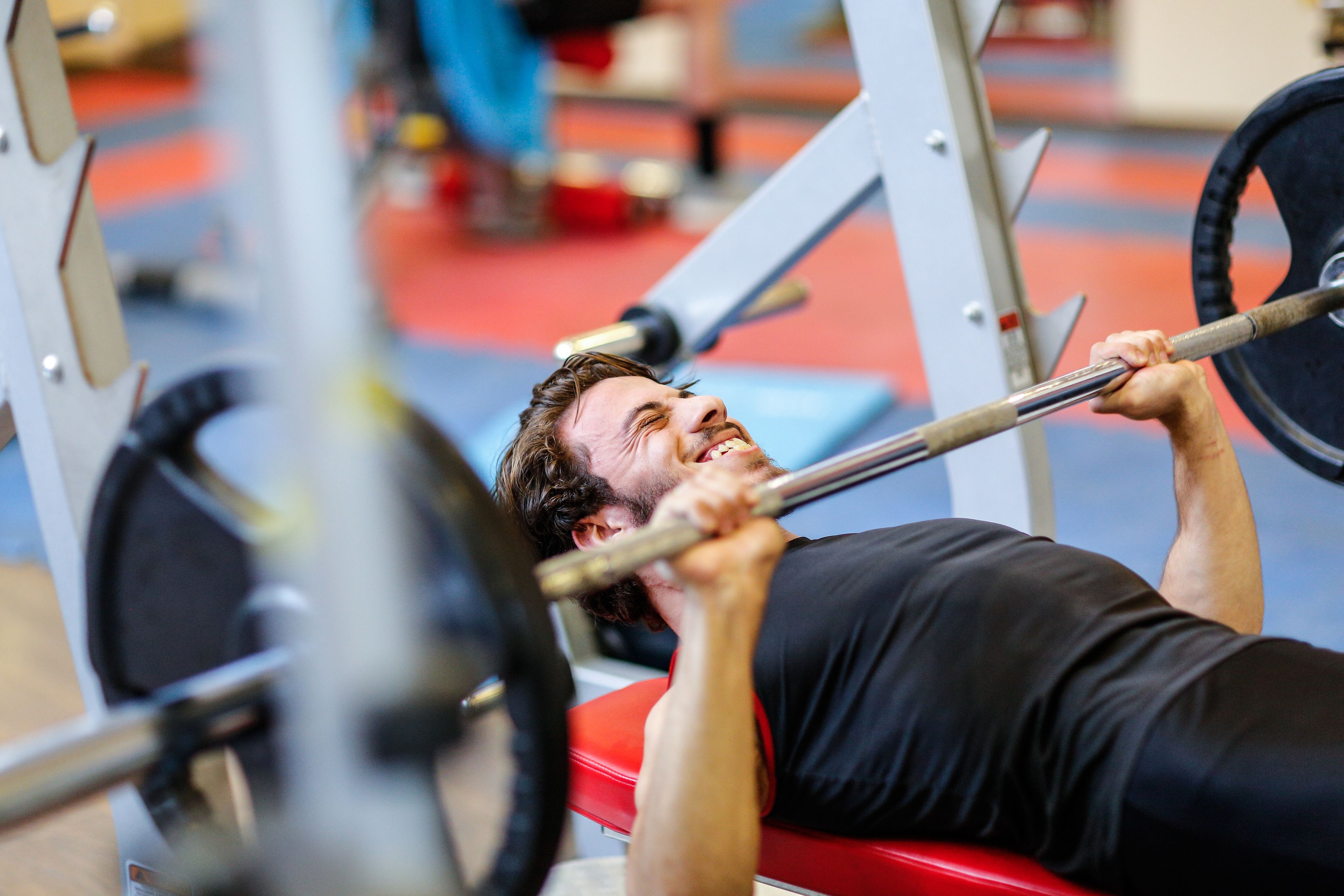 A person using a bench press machine in a gym with a red bench and weight plates.