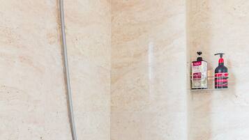 A bathroom with a shower, a handheld showerhead, a wall-mounted faucet, and two toiletry bottles on a shelf.