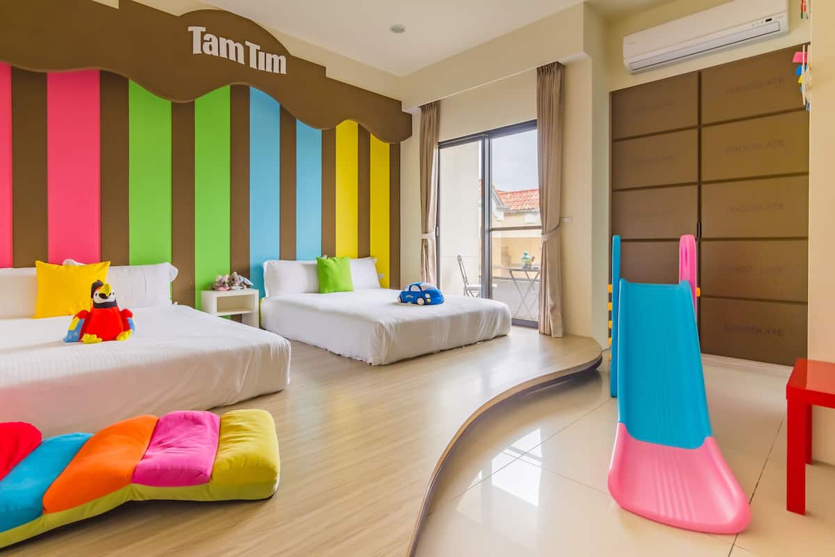 A hotel room with two beds, colorful pillows, a play area with a slide, and a view of the outside.