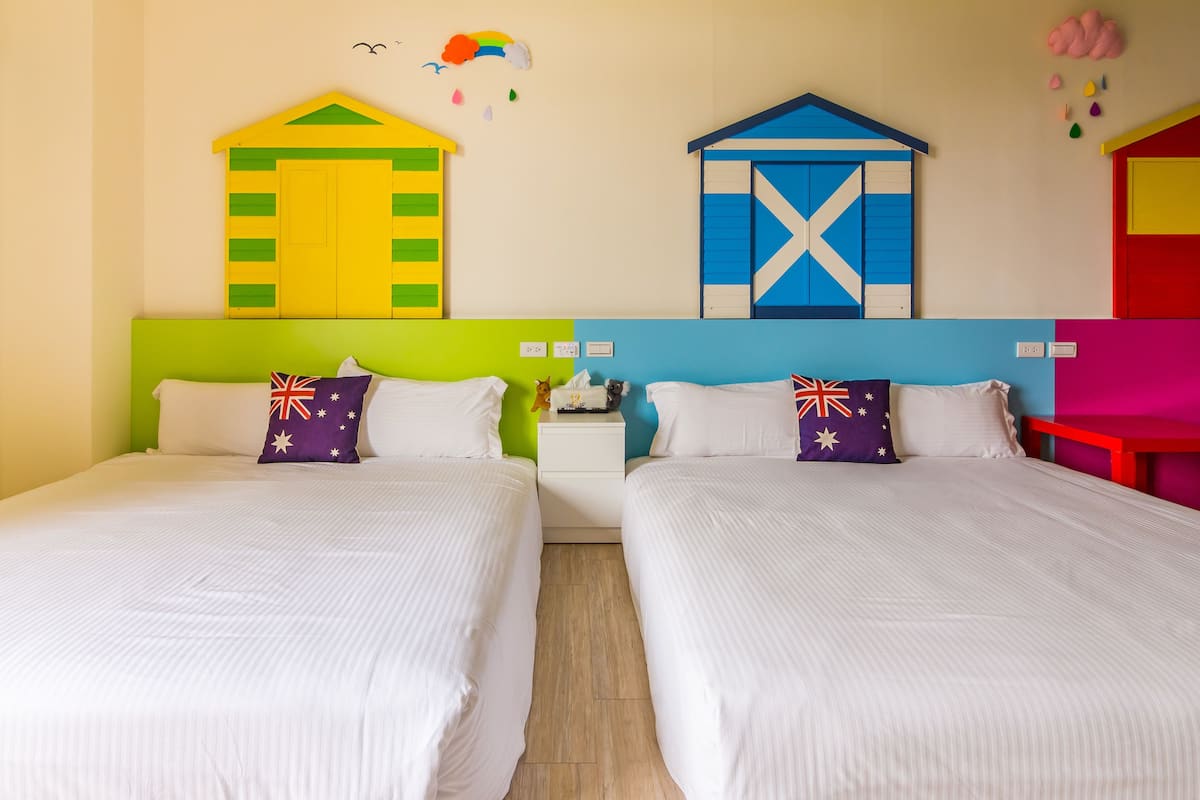 Two twin beds with white bedding, colorful pillows, and a nightstand with a lamp between them.