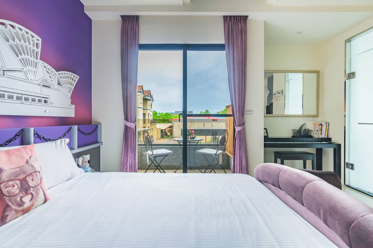 A hotel room with a bed, a desk, a chair, and a view of the outside.