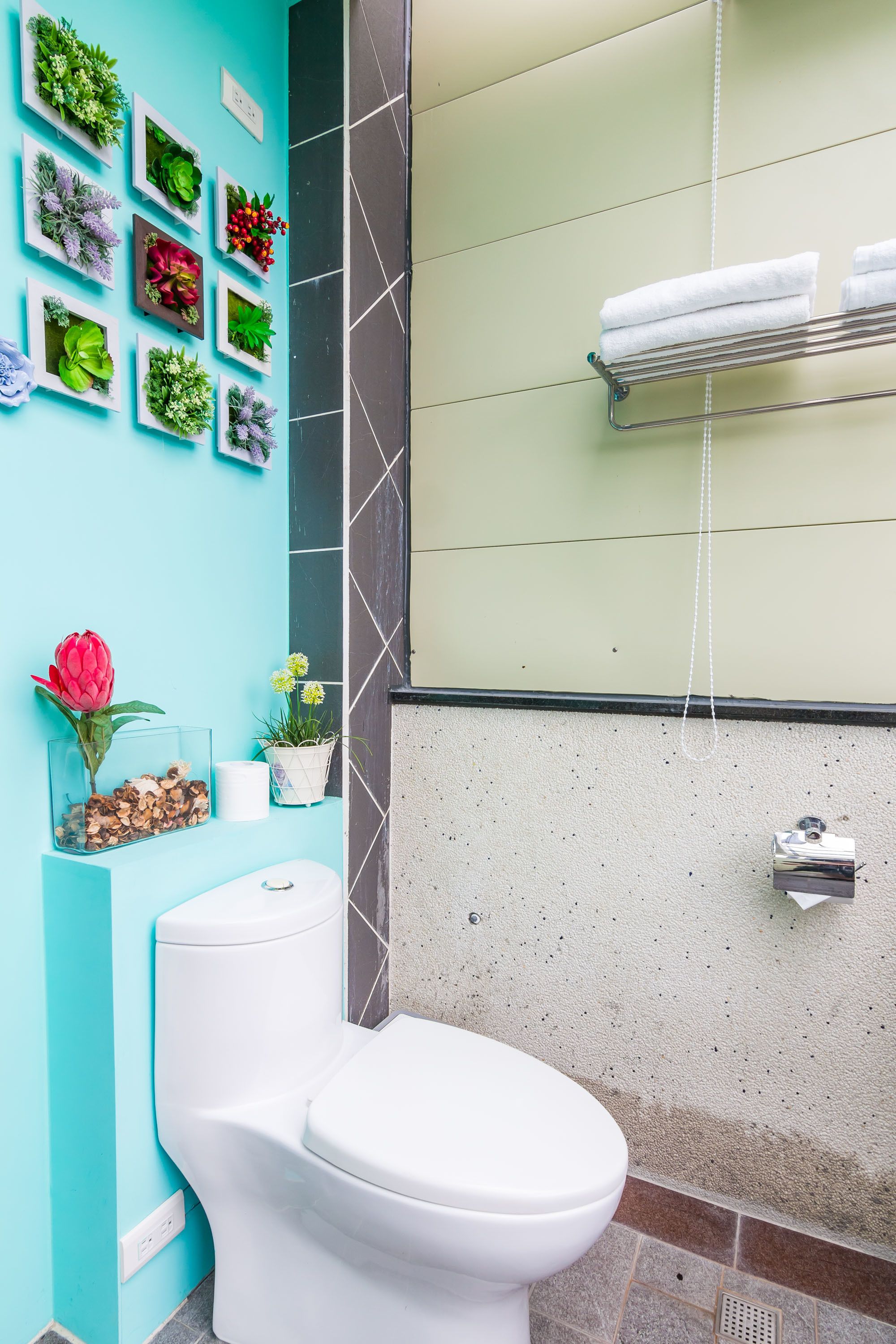A bathroom with a white toilet, a towel rack with folded towels, and a wall decorated with various potted plants.