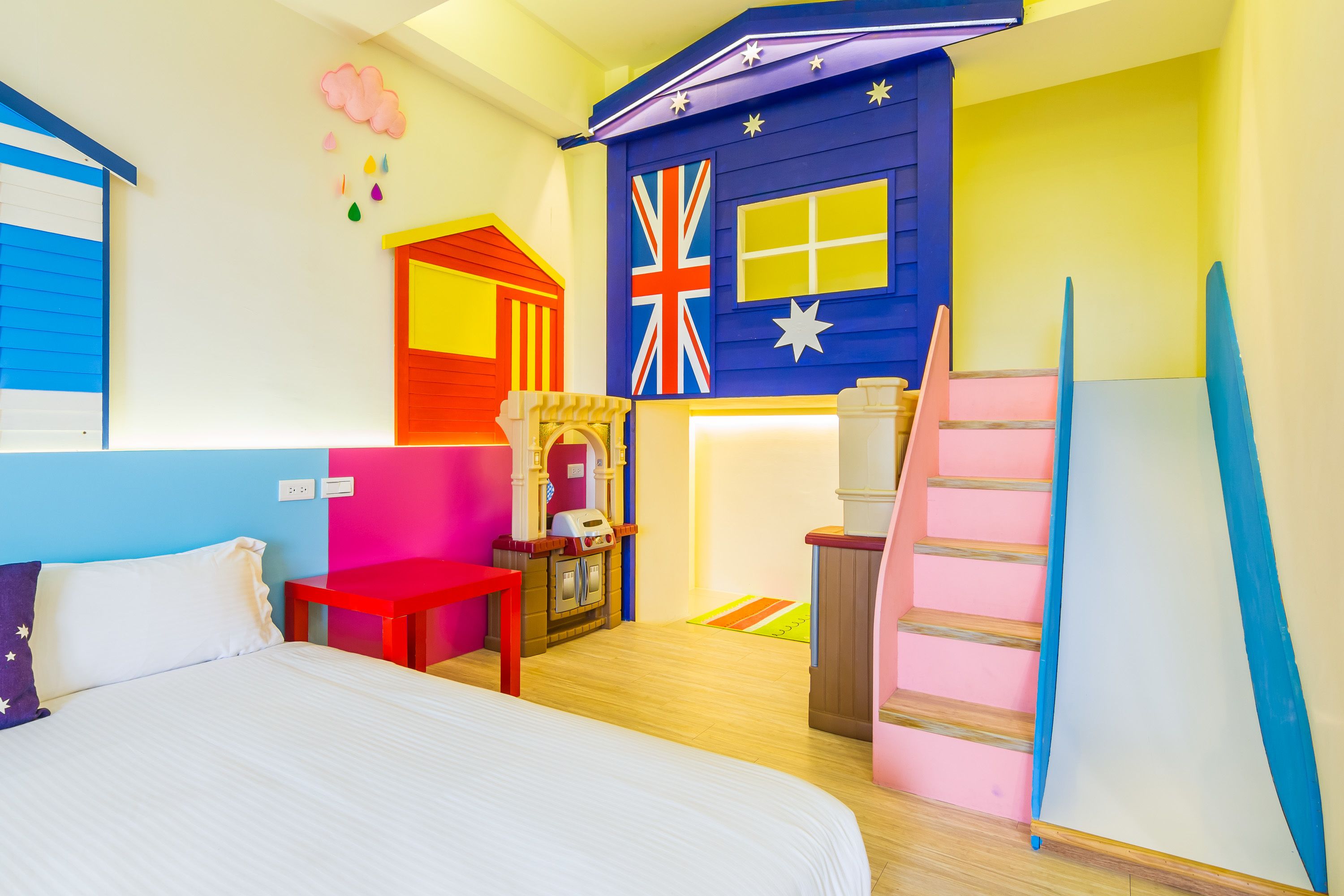 A room with a bed, a red table, a fireplace, a British flag, and a staircase.