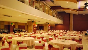 Un amplio salón de banquetes con varias mesas redondas, cada una cubierta con manteles blancos y cintas rojas.
