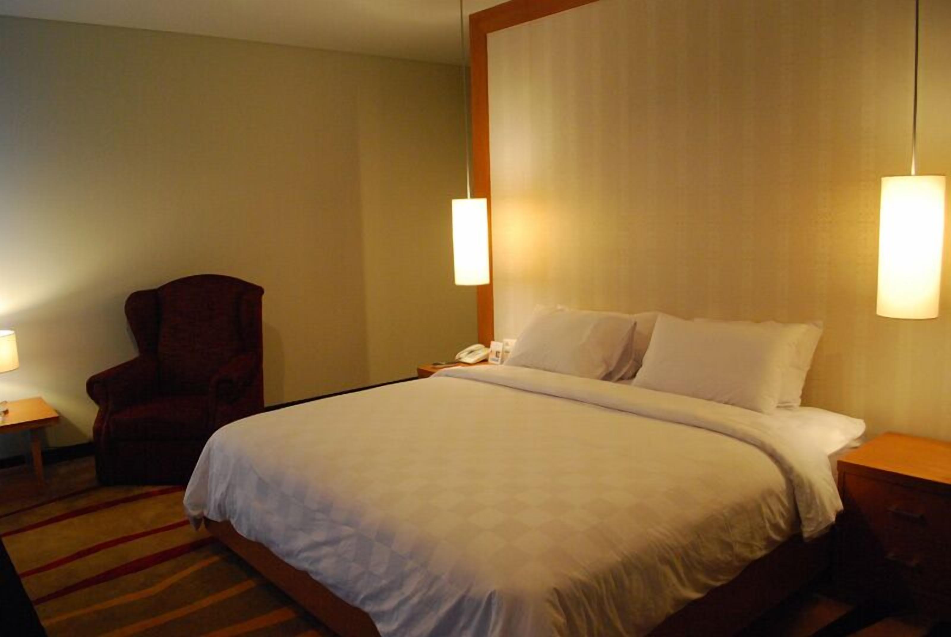 A hotel room with a large bed, a chair, a bedside table with a lamp, and a nightstand with a phone.