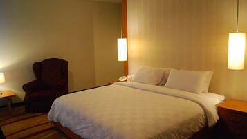 A hotel room with a large bed, a chair, a bedside table with a lamp, and a nightstand with a phone.