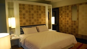 Una habitación de hotel con una cama grande, dos lámparas de noche, una mesita de noche con un teléfono y un papel tapiz estampado.
