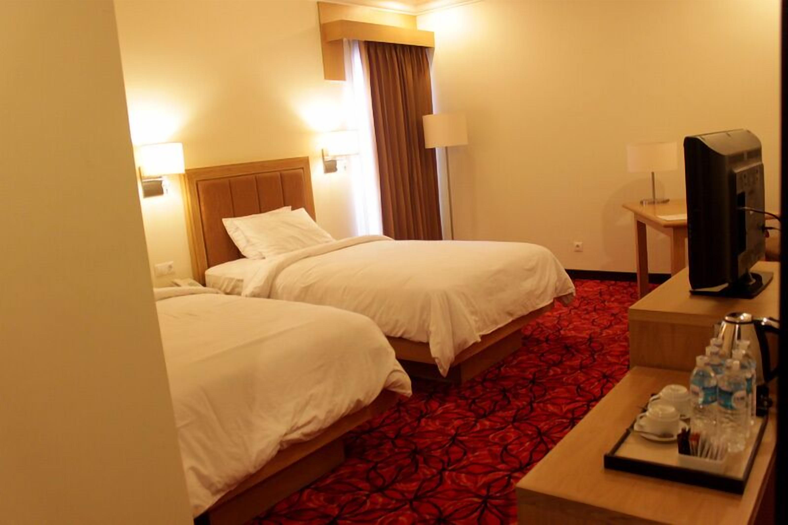 A hotel room with two beds, a TV, a desk with a tray of toiletries, and a red carpet.