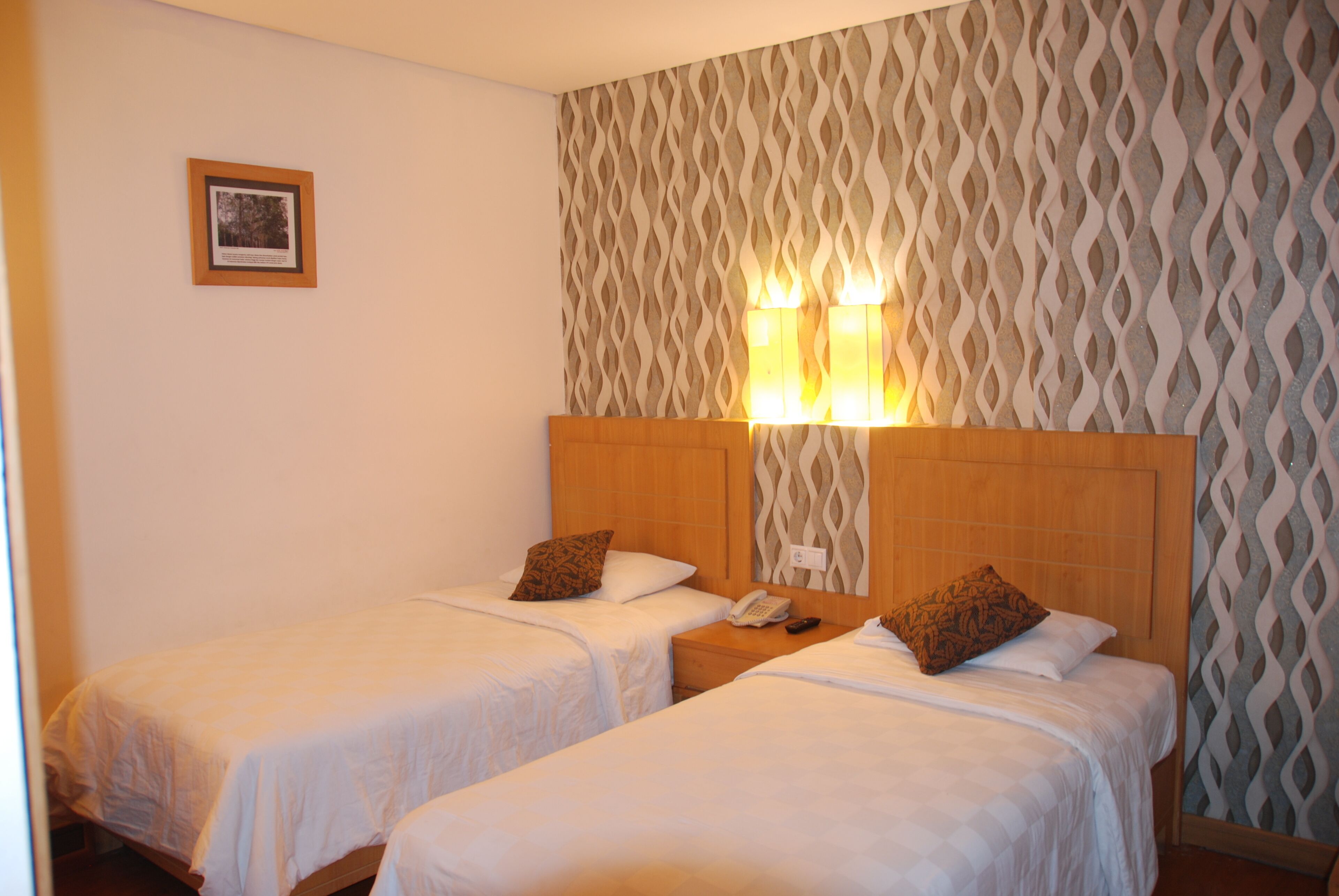 A hotel room with two single beds, a wooden headboard, a patterned wall, and a framed picture on the wall.