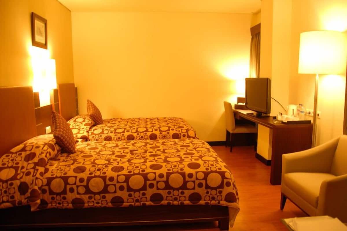 A hotel room with two beds, a desk, a chair, and a television.
