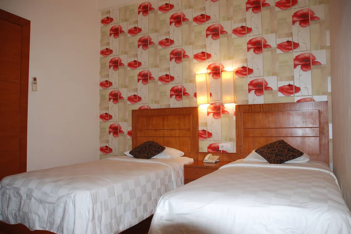 A hotel room with two single beds, a wooden headboard, and a floral wallpaper design.