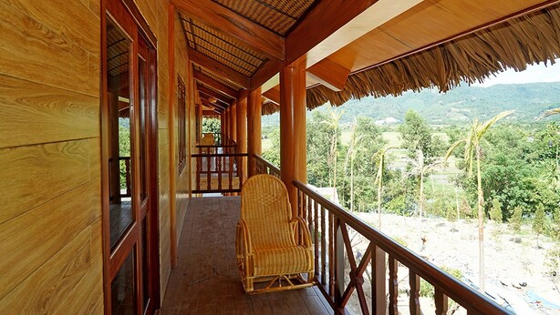 Un couloir en bois, avec une chaise en osier sur un balcon donnant sur un paysage montagneux.