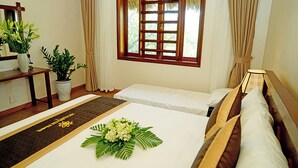 Une chambre d’hôtel avec un lit, une petite table sur laquelle est posé un vase de fleurs, une fenêtre avec des rideaux et une plante en pot.