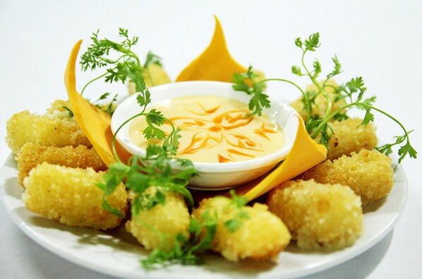 A plate of breaded and fried food items, garnished with parsley, accompanied by a bowl of dipping sauce.