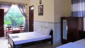 A bedroom with a bed, a desk, and a chair. There is a window with curtains, a painting on the wall, and a door. - Nhat Lan Resort (Phu Quoc)