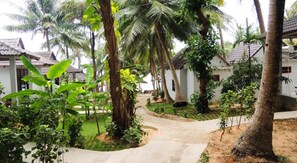 A pathway leading to a row of white buildings with thatched roofs, surrounded by lush greenery and palm trees. - Nhat Lan Resort (Phu Quoc)