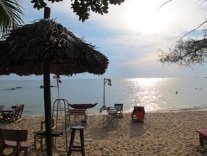 A beach with a thatched umbrella, lounge chairs, and a table set up for dining. - Nhat Lan Resort (Phu Quoc)