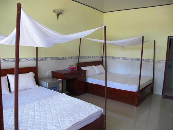 A room with two beds, each with a canopy. There is a small desk with a chair and a nightstand. - Nhat Lan Resort (Phu Quoc)