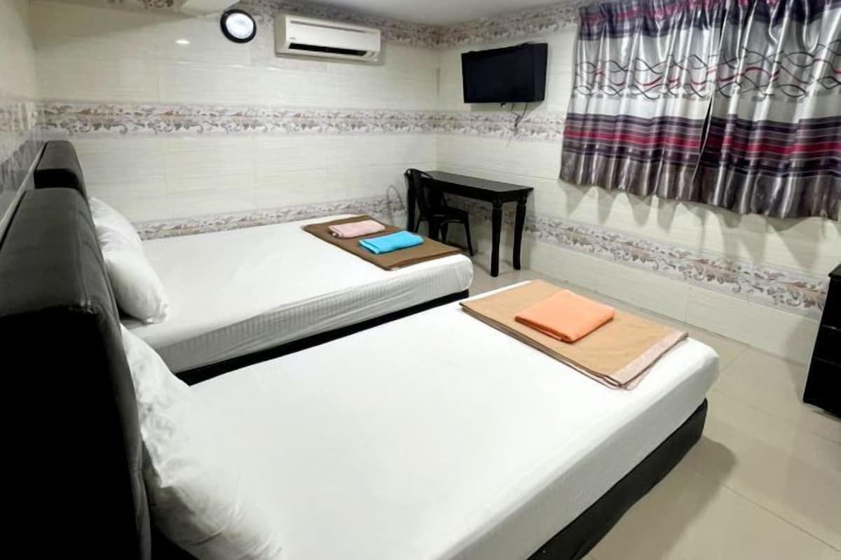 Habitación de hotel con dos camas, un escritorio, un televisor y un ventanal con cortinas.