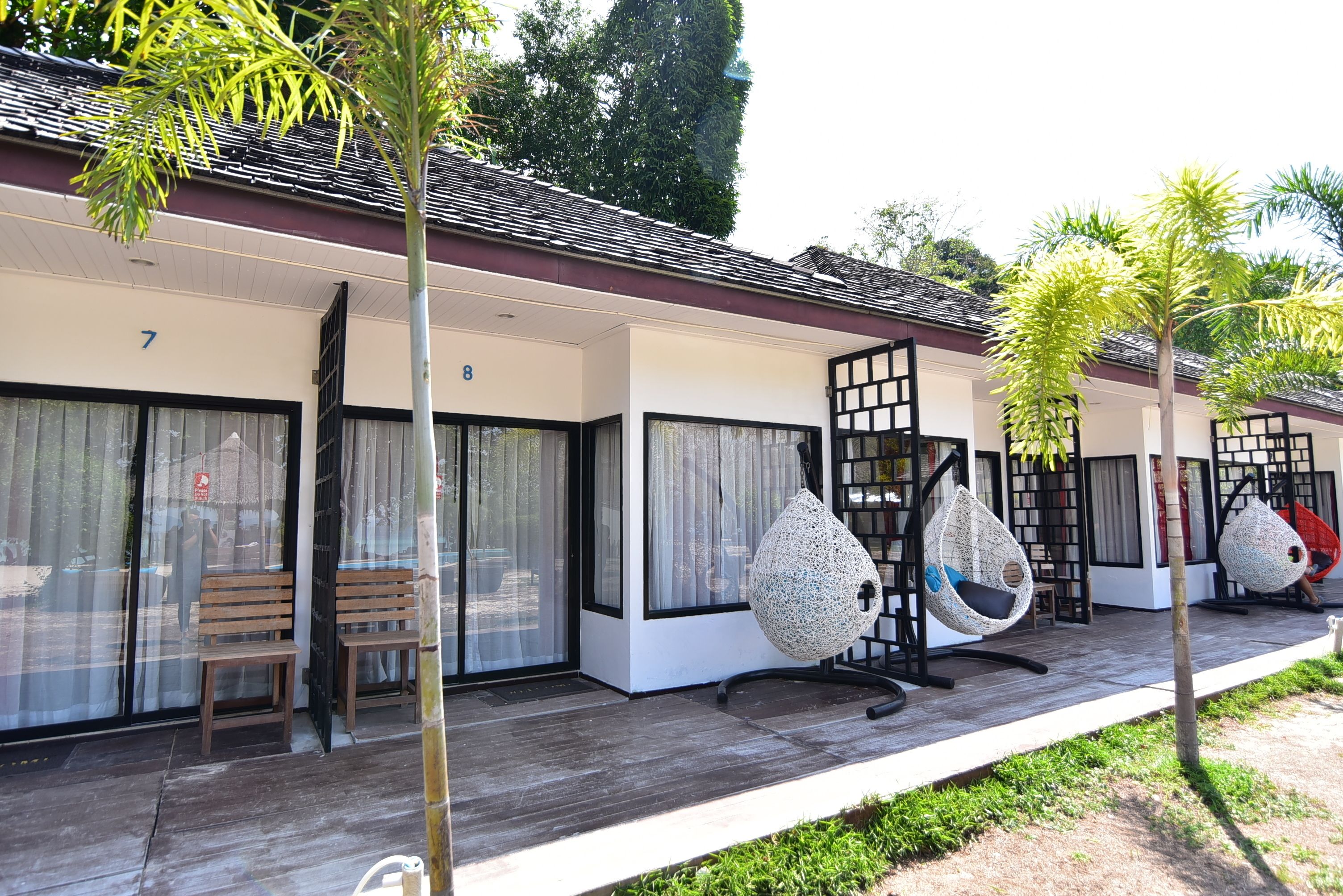 A row of rooms with large windows, wooden benches, and hanging chairs.