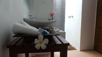 Un baño con bañera, una toalla, una flor y una mesita.