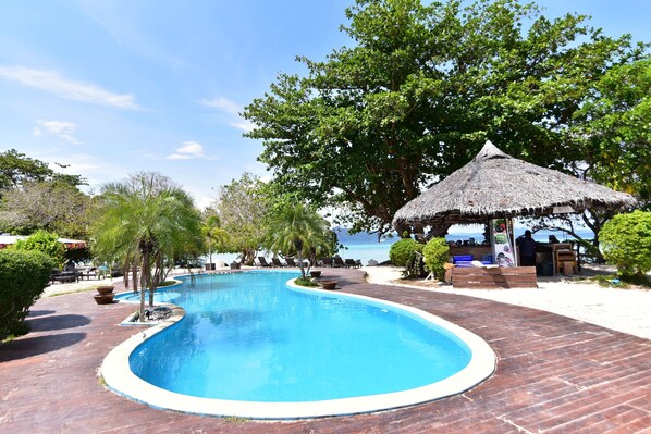 A swimming pool with a curved edge, surrounded by a wooden deck and a thatched-roof structure. - Reef Resort (Ko Kradan)
