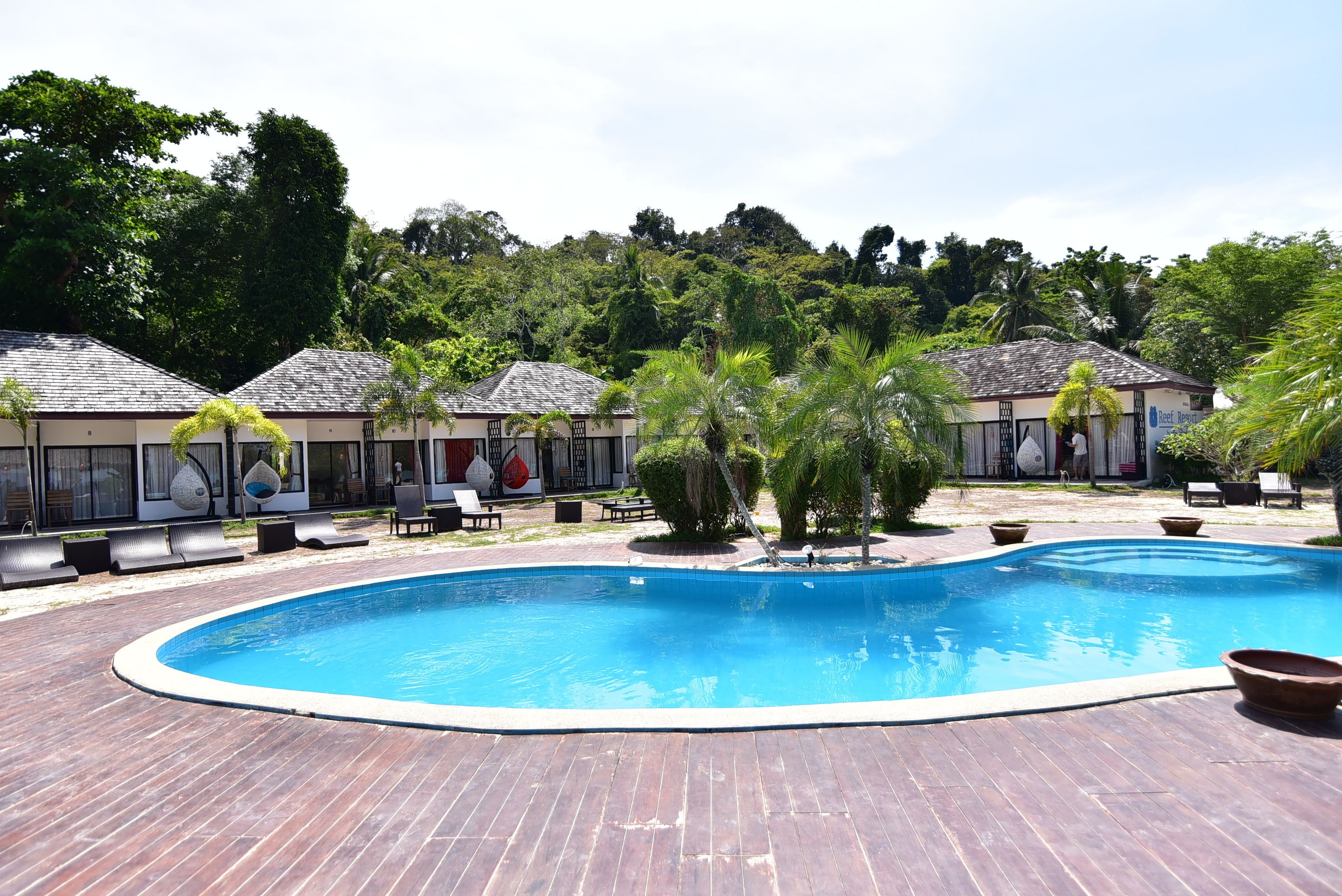 Una piscina con sillas de descanso y un área techada con un letrero que dice 'Tropical Resort'.