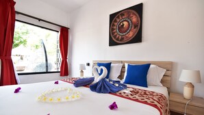 A neatly made bed with a swan-shaped towel, white and blue pillows, and a red and white patterned blanket. - Reef Resort (Ko Kradan)