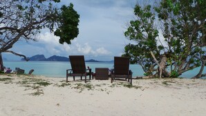 Two wicker lounge chairs facing a beach with clear turquoise water and distant mountains. - Reef Resort (Ko Kradan)