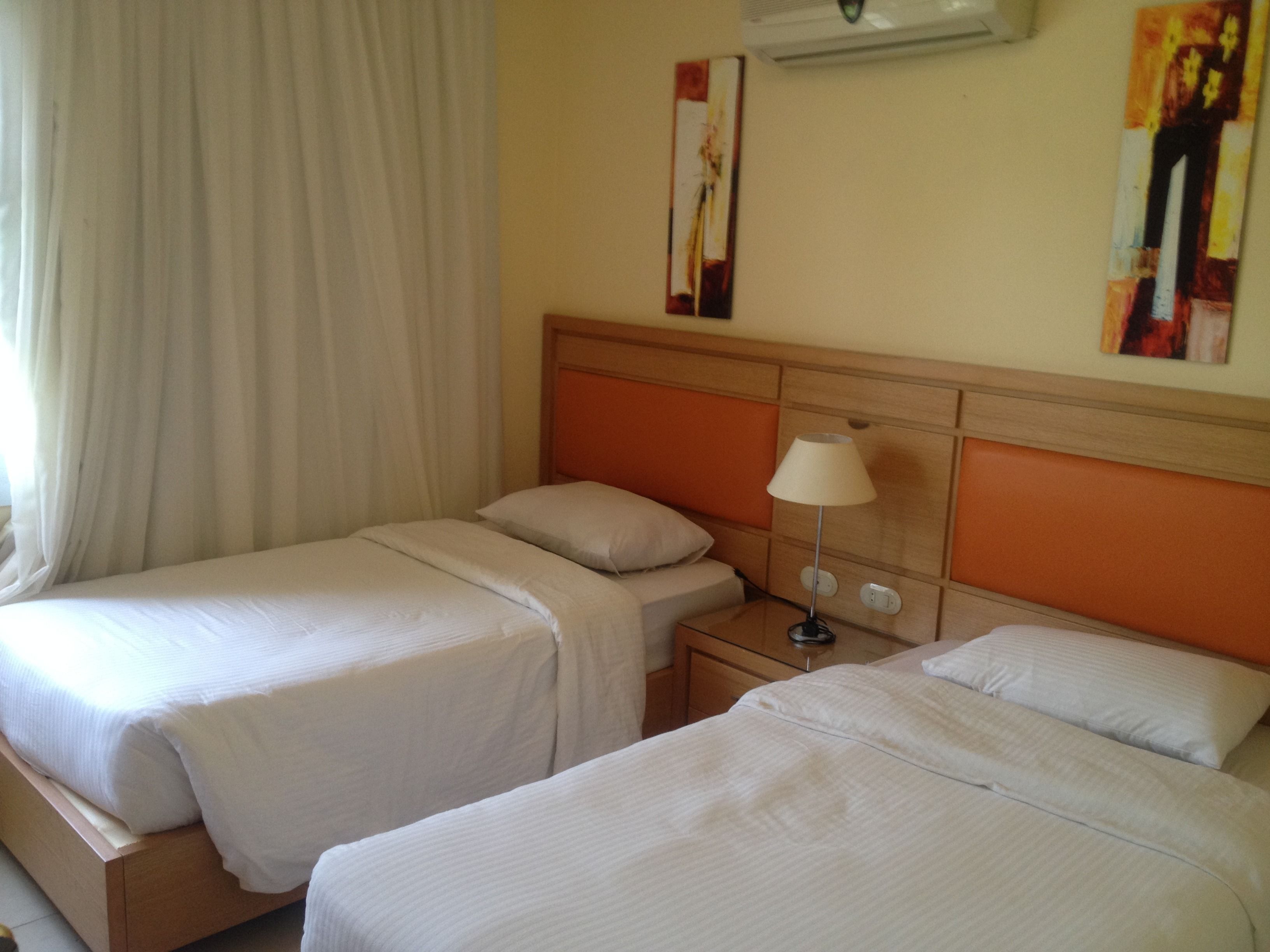 A hotel room with two beds, a nightstand, a lamp, and artwork on the walls.