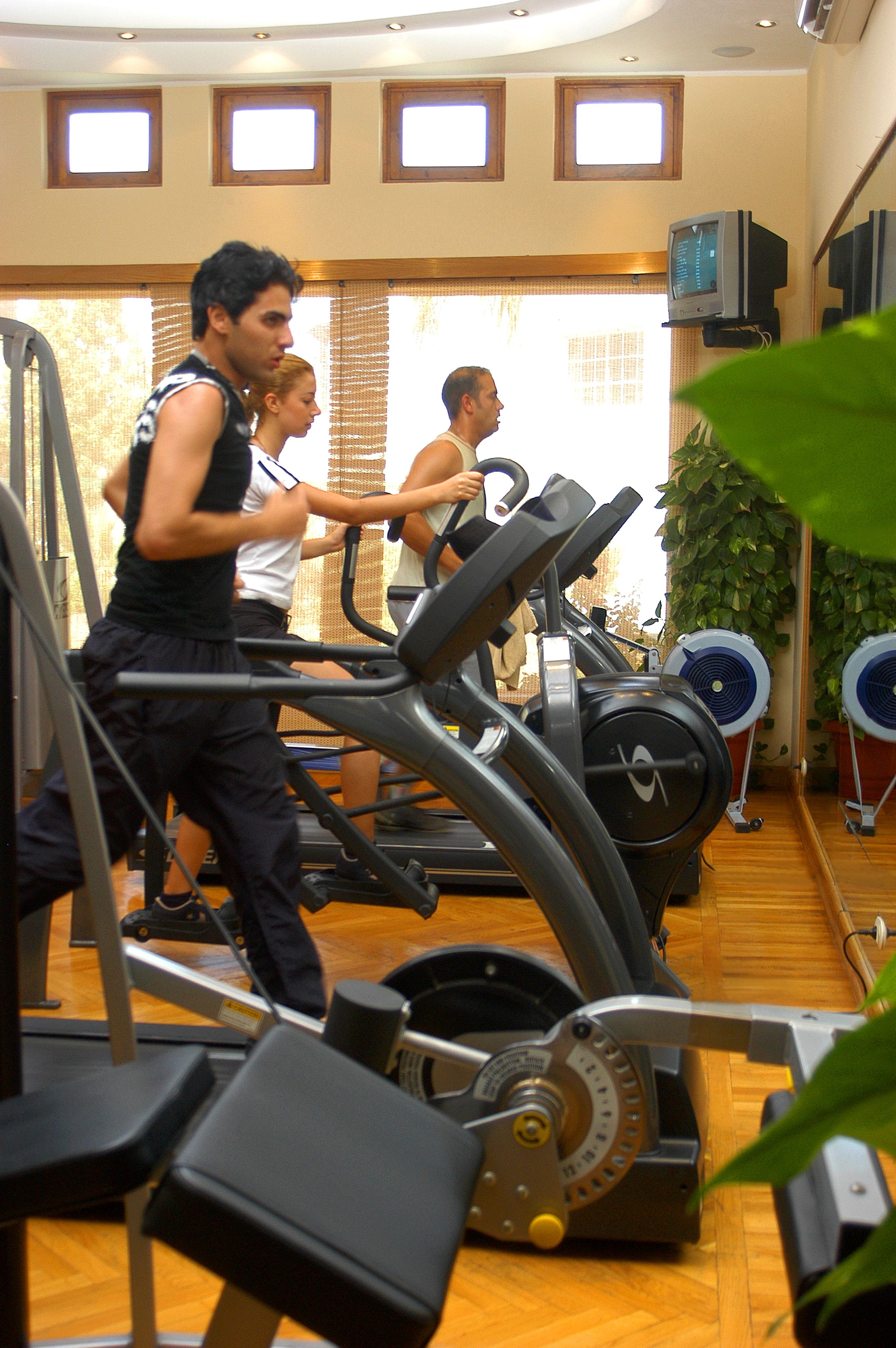 A gym with treadmills, exercise equipment, and a large window with blinds.
