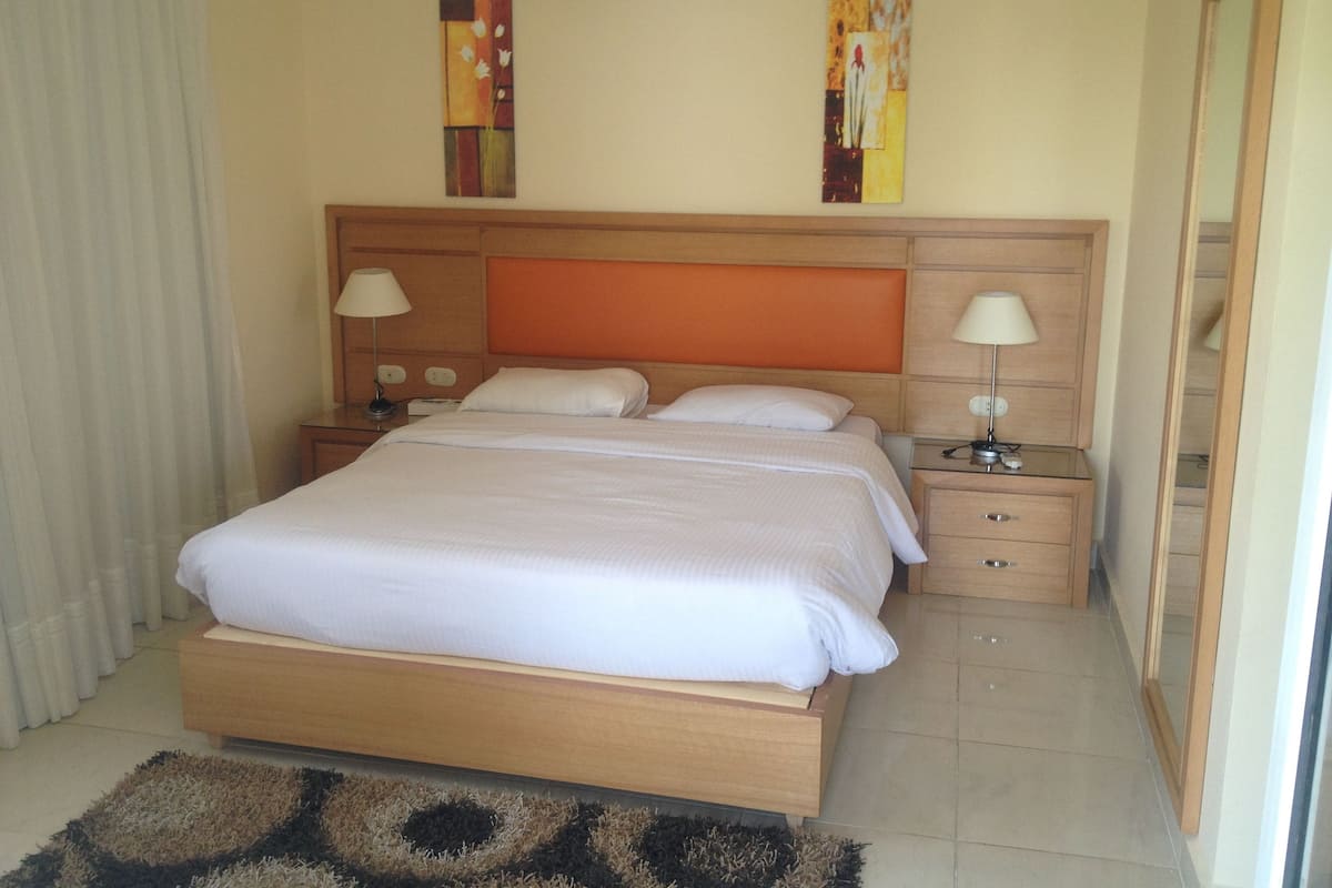 A neatly made bed with a wooden headboard, two bedside tables with lamps, and a small rug on the floor.