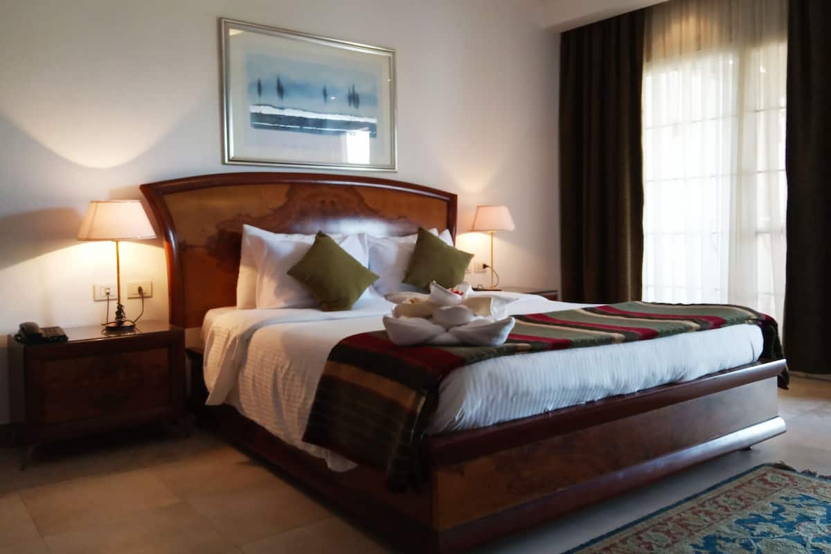 A hotel room with a large bed, two bedside lamps, a nightstand, a framed picture on the wall, and a window with curtains.
