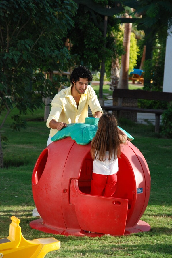 Un hombre y un niño jugando en una estructura esférica roja al aire libre.