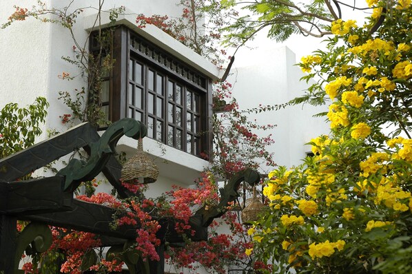 A traditional building with a white facade, a window with dark wooden shutters, and a balcony with hanging baskets.