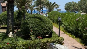 A landscaped garden with palm trees, a stone pathway, and a view of the sea. - Lito Beach (Platanias)