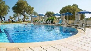 A swimming pool with lounge chairs and umbrellas, surrounded by trees and a stone wall. - Lito Beach (Platanias)