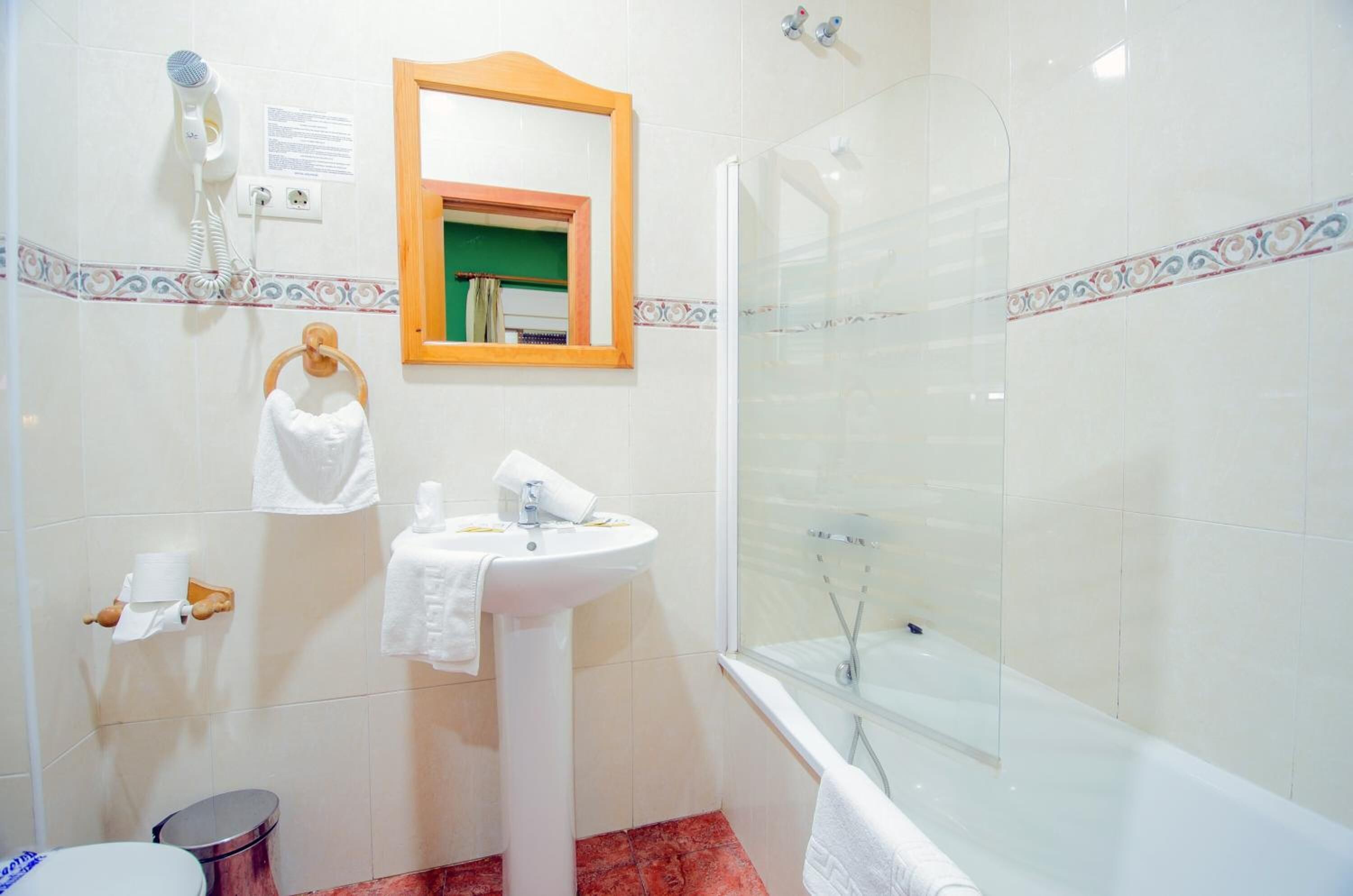 Un baño con lavamanos, espejo, toallero, ducha e inodoro.