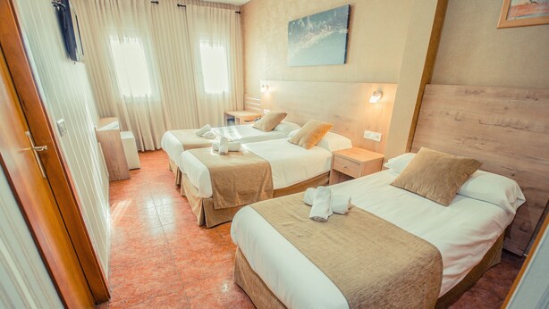 A hotel room with three beds, a wooden headboard, a painting on the wall, and a window with curtains. - Hotel Solymar (Málaga)