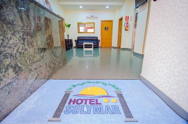 A hotel lobby with a marble reception desk, a blue sofa, and a reception area. - Hotel Solymar (Málaga)