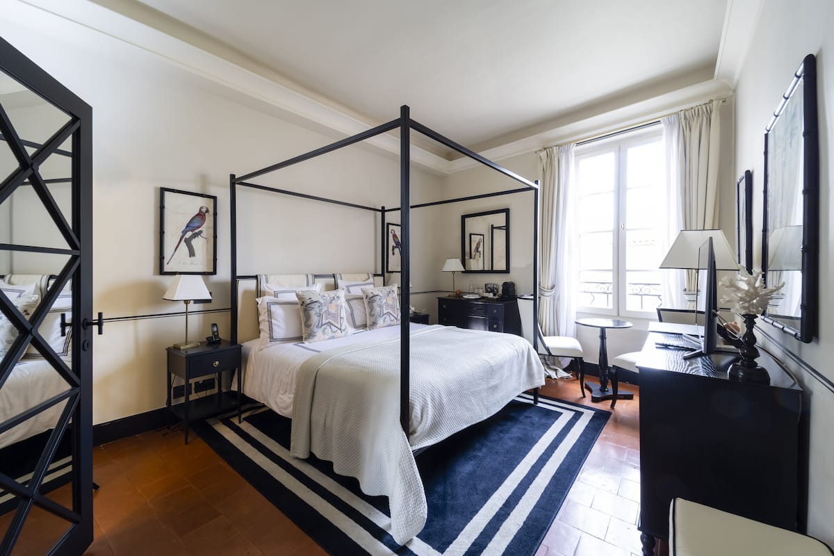 Un lit à baldaquin avec une couvre-lit blanche, une table de chevet noire avec une lampe, un bureau avec une lampe et une chaise.