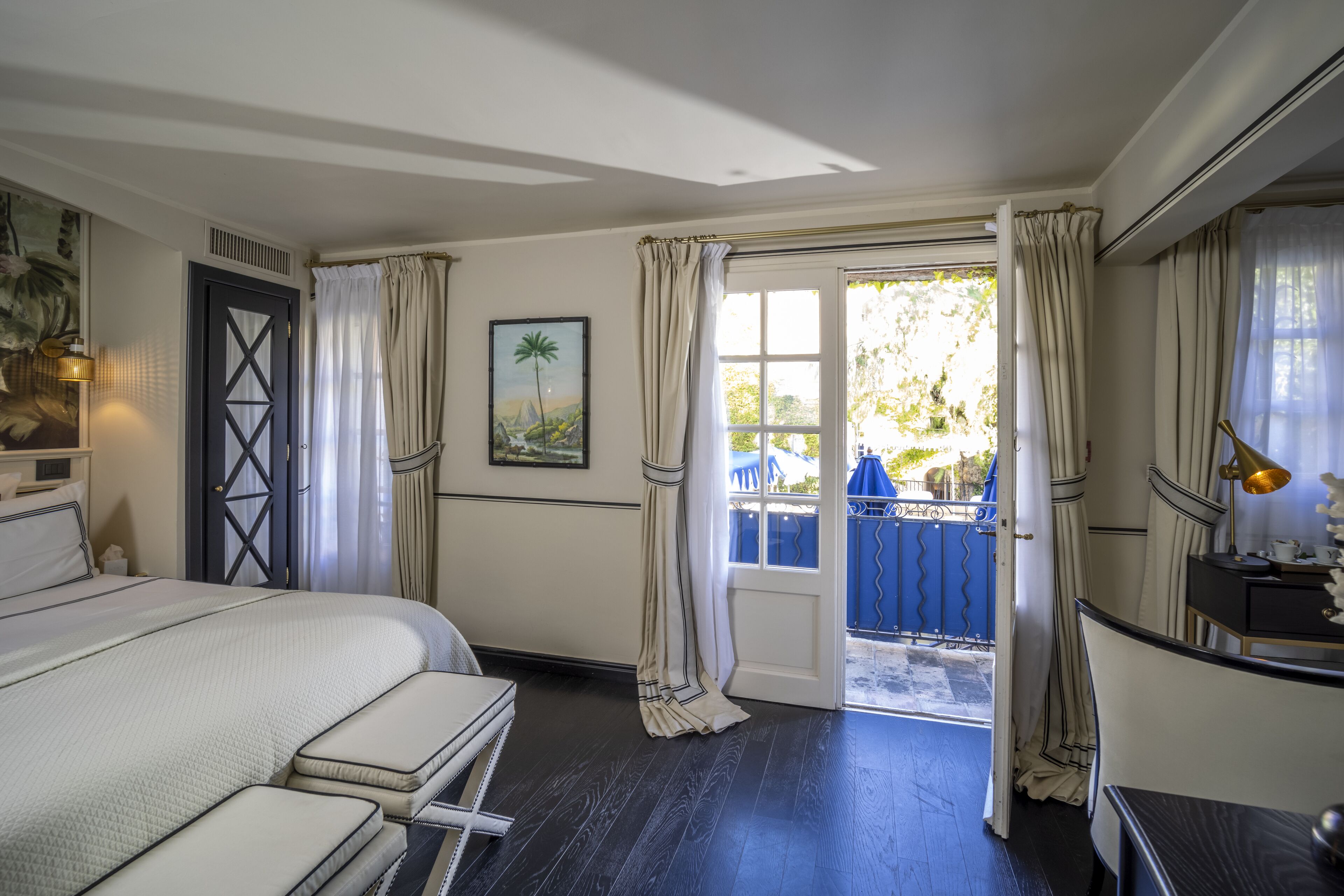 Ein Hotelzimmer mit Bett, Schreibtisch, Stuhl, einem Fenster mit Vorhängen und einer Tür zu einem Außenbereich.