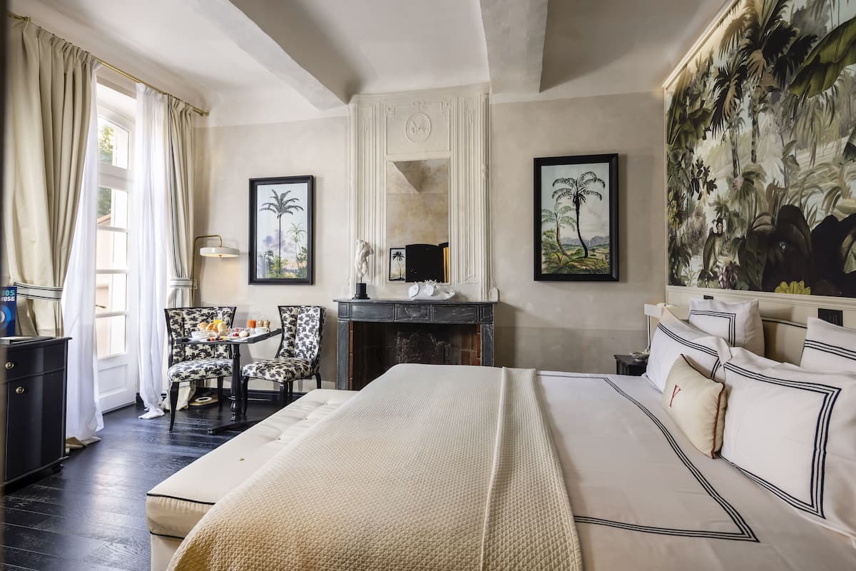 Une chambre d’hôtel avec un grand lit, un bureau avec une chaise, une cheminée et une fresque murale aux motifs tropicaux.