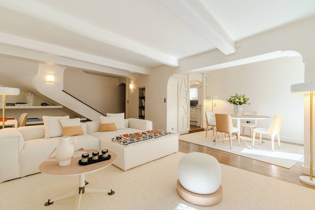 Un salon moderne comprenant un canapé, une table basse et un pouf, un coin repas avec des chaises et une table, et un escalier menant à un autre niveau.