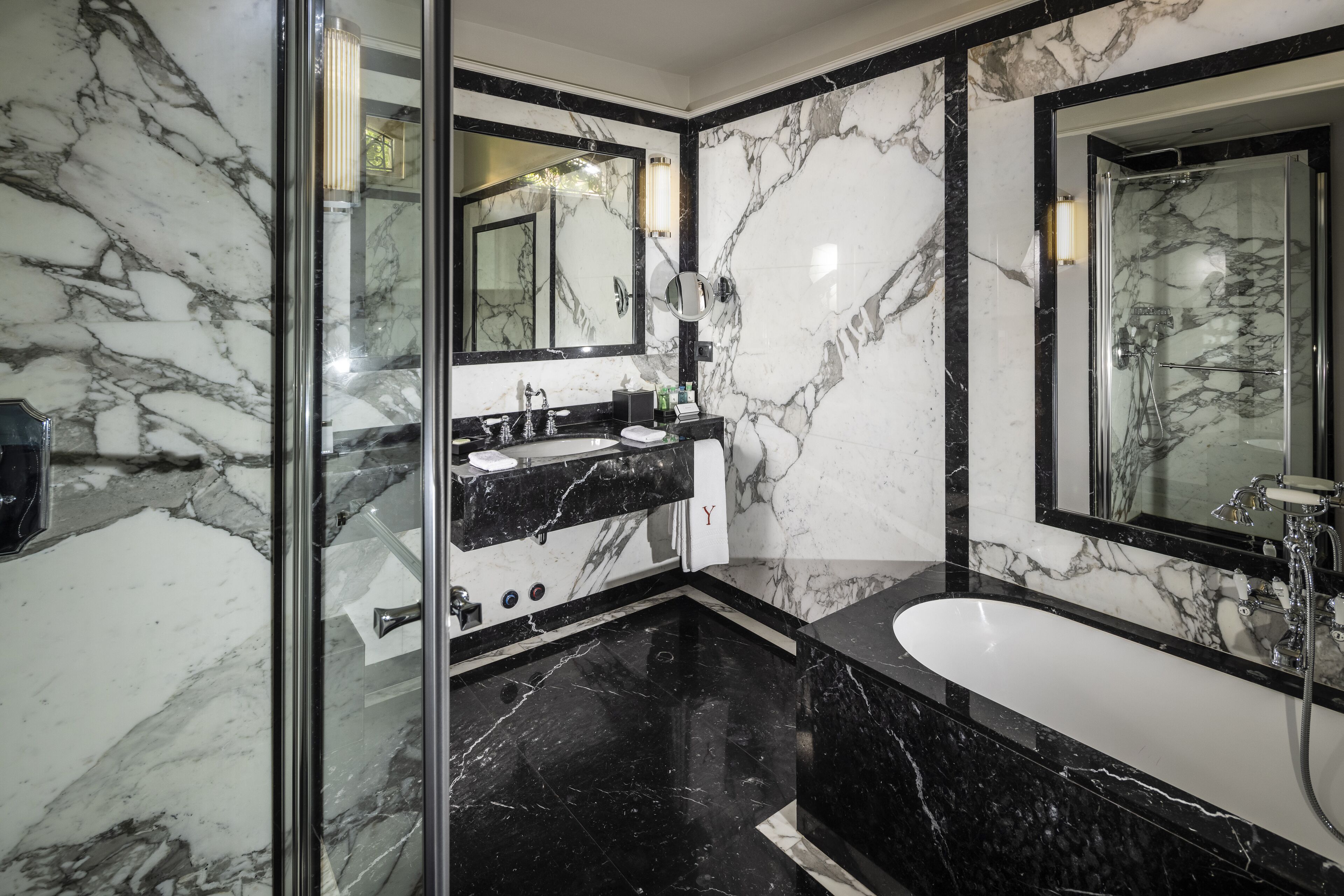 A modern bathroom with marble walls, a black countertop, a large mirror, and a glass-enclosed shower area.